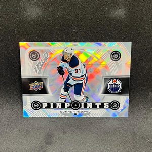 以下が含まれることがあります： エドモントン・オイラーズのユニフォームを着たコナー・マクデビッドをフィーチャーしたホッケーのトレーディングカード。カードは「MVP」と「PINPOINTS」の文字が入った銀色のホログラフィック背景です。Upper DeckとOilersのロゴも表示されています。