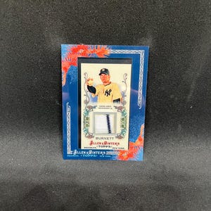 May include: A baseball trading card featuring a player in a New York Yankees uniform. The card has a blue border with floral accents and includes the text "ALLEN & GINTER'S" and "BURNETT". A patch of fabric is visible.