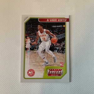 May include: A De'Andre Hunter basketball card from the Panini Threads 2019-20 series. The card features Hunter in his Atlanta Hawks uniform, dribbling a basketball. The card has a green and white border with the Hawks logo.