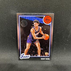 May include: A Koby Brea Phoenix Suns basketball trading card. The card features a player in a purple and orange uniform holding a basketball. The card has a silver border, the Topps logo, and the Suns logo.