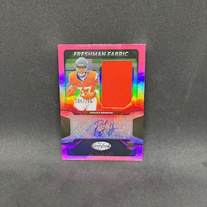 May include: A rectangular sports trading card featuring a Denver Broncos player in an orange jersey with the text Freshman Fabric, 204/299, and Denver Broncos. The card includes an orange fabric swatch, a blue ink autograph, and a 2025 Certified logo.