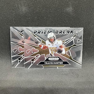 May include: A pair of sports trading cards featuring a football player in a white and gold uniform. The cards have a silver and black geometric design with the text "PRIZM BREAK" and the player's name, Travis Hunter.
