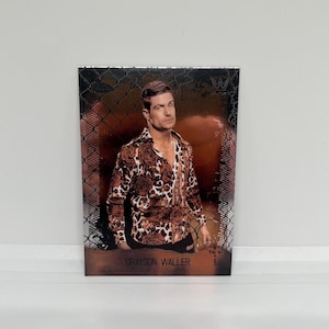 May include: A trading card featuring Grayson Waller. The card shows a man wearing a brown and black patterned shirt and a gold chain. The card has a metallic finish and the name "Grayson Waller" is printed at the bottom.