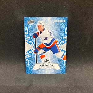 Può includere: Una carta sportiva rettangolare raffigurante un giocatore di hockey in uniforme bianca, blu e arancione con il numero 32. La carta presenta un motivo di sfondo ghiacciato blu e bianco, il testo ROOKIE e il nome KYLE MACLEAN NEW YORK ISLANDERS-C.