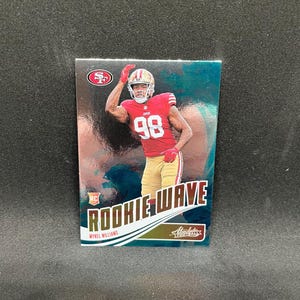 May include: A football trading card featuring Mykel Williams in a red jersey with the number 98. The card has the text "ROOKIE WAVE" and the San Francisco 49ers logo. The background is a teal and silver gradient.