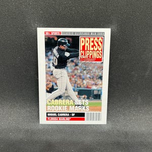 May include: A baseball card featuring Miguel Cabrera of the Florida Marlins. The card has the text "PRESS CLIPPINGS" and "CABRERA SETS ROOKIE MARKS". The card is white with red and black text and a photo of Cabrera in action.