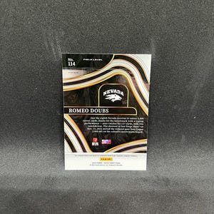 May include: A sports trading card featuring Romeo Doubs, with the Nevada logo and the text "ROMEO DOUBS." The card has a black and gold design with the number 114. The card also includes text about Doubs' achievements.