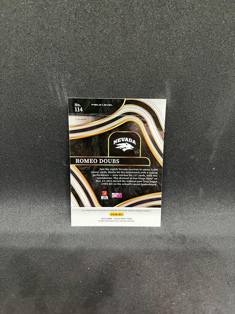 May include: A sports trading card featuring Romeo Doubs, with the Nevada logo and the text "ROMEO DOUBS." The card has a black and gold design with the number 114. The card also includes text about Doubs' achievements.