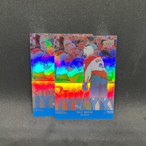 Könnte beinhalten: Zwei identische Upper Deck Eishockey-Sammelkarten mit Cale Makar in einem weißen, roten und blauen Colorado-Trikot. Die Karten haben ein holografisches, regenbogenfarbenes Finish mit dem Text CALE MAKAR und COLORADO am unteren Rand.