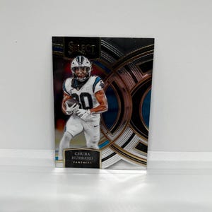 May include: A silver and black football trading card featuring a player in a blue and black uniform with the text "SELECT" in gold lettering. The player's name is "CHUBA HUBBARD" and the team is "PANTHERS".