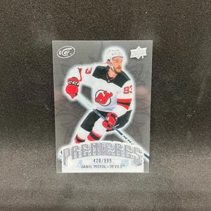 May include: A rectangular Upper Deck Ice hockey trading card featuring Daniil Misyul of the New Jersey Devils. The card displays the player in a white, red, and black uniform holding a hockey stick, with the text PREMIERES, 420/999, and his name.