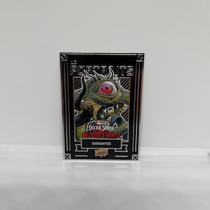 May include: A trading card featuring Gargantos from Doctor Strange in the Multiverse of Madness. The card has a black border with the word "Portraits" at the top. The image shows a green monster with a large red eye.