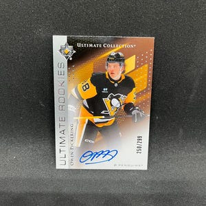 May include: A rectangular Ultimate Collection hockey trading card featuring Owen Pickering in a black and yellow Pittsburgh Penguins jersey. The card includes a blue ink autograph, the text Ultimate Rookies, and the serial number 250/299.