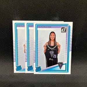 May include: Three sports trading cards featuring Kaitlyn Chen. The cards have a white border with blue and purple accents. The cards display a photo of Kaitlyn Chen holding a black jersey with the number 25. The cards also have the text "RATED ROOKIE" and "DONRUSS".