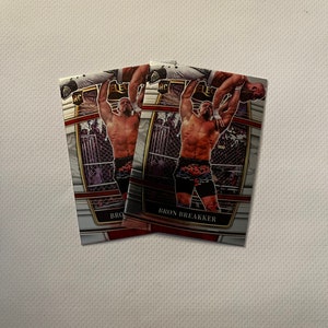 May include: Three trading cards featuring a wrestler in a wrestling ring. The wrestler is wearing black and orange wrestling trunks. The cards are silver with red and gold accents. The text on the cards reads "Bron Breakker".