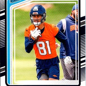 Può includere: Una carta collezionabile di football dei Denver Broncos con Devaughn Vele. La carta ha un bordo blu e include il testo "Rated Rookie" e "Donruss". Vele indossa una maglia arancione con il numero 81 e un casco blu.