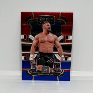 May include: A wrestling trading card featuring Bron Breakker. The card has a red, white, and blue design with a gold border. The card features a photo of Bron Breakker in the ring.