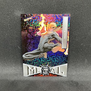 May include: A Marvel Metal Universe trading card featuring Iron Fist. The card has a holographic background with a dynamic illustration of the character in action. The card has the text "Iron Fist" and "Metal" on it.