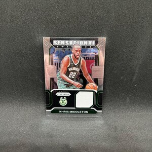 Puede incluir: Una tarjeta de baloncesto coleccionable con Khris Middleton con el uniforme de los Bucks de Milwaukee. La tarjeta tiene un diseño verde, negro y blanco con las palabras "Sensational Swatches" en la parte superior y "Prizm" en la parte inferior.