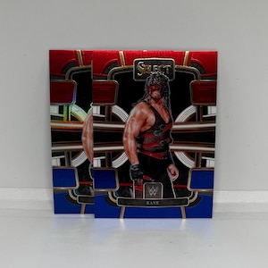 Puede incluir: Dos cartas de intercambio con un luchador con una máscara roja y un atuendo negro y rojo. Las cartas son rojas, doradas y azules con el texto "SELECT" y "KANE" en ellas.