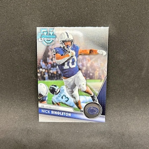 May include: A Bowman Chrome trading card featuring a football player in a blue jersey with the number 10, white pants, and a white helmet. The card displays the text Nick Singleton, RB, Penn State, and includes a circular team logo emblem.