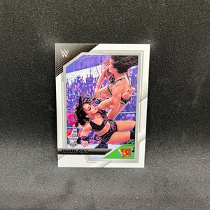 Könnte beinhalten: Sammelkarte mit Roxanne Perez in Aktion. Die Karte hat einen weißen Rand mit dem WWE-Logo oben links und der Bezeichnung Rookie Card. Das Bild zeigt zwei Wrestlerinnen in einer dynamischen Pose, mit einem Publikum im Hintergrund.