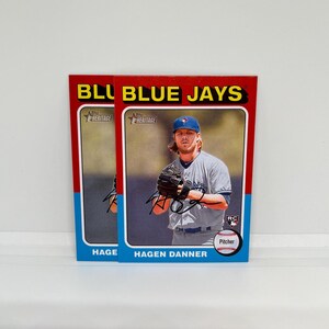 May include: Two baseball cards featuring Hagen Danner of the Toronto Blue Jays. The cards have a red border with the words "BLUE JAYS" in yellow. The player is wearing a blue cap and a gray jersey. The word "Pitcher" is visible.