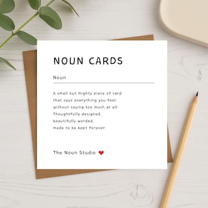 Square white greeting card on kraft envelope with pencil and greenery, featuring the text 'NOUN CARDS – A small but mighty piece of card that says everything you feel, without saying too much at all' from The Noun Studio. Minimalist definition-style card mockup for Etsy