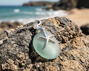 May include: A pendant necklace featuring a smooth, frosted sea glass stone in a pale mint green color. A polished silver-toned starfish charm is securely attached to the front of the glass. The pendant hangs from a simple silver-toned chain.
