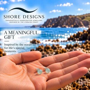 Puede incluir: Dos pendientes de bot&oacute;n peque&ntilde;os, redondos y de color azul claro con acabado mate. El texto en la imagen dice: SHORE DESIGNS, THOUGHTFULLY HANDCRAFTED JEWELLERY INSPIRED BY THE CORNISH COAST. A MEANINGFUL GIFT, Inspired by the ocean for life's special moments.