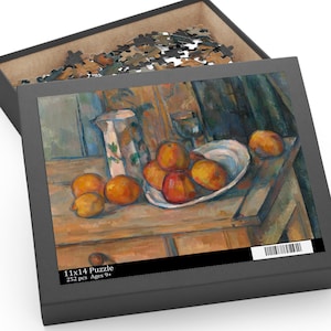 May include: A 252-piece puzzle in a black box, featuring a still life painting of oranges, a white plate, a pitcher, and a glass. The box is labeled "11x14 Puzzle" and "Ages 9+". The puzzle pieces are visible inside the open box.