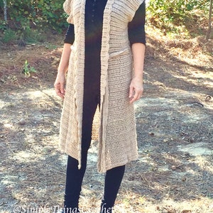 Puede incluir: Un c&aacute;rdigan largo de crochet beige con cuello chal y detalles de flecos. El c&aacute;rdigan se lleva sobre una camiseta negra y leggings negros.