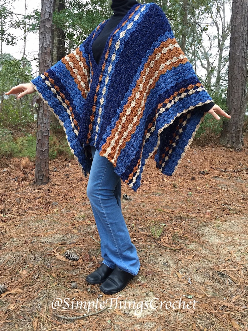 Puede incluir: Un poncho de ganchillo azul, marr&oacute;n y crema. El poncho tiene un patr&oacute;n de rayas con un dise&ntilde;o de cuello en V. La persona de la imagen lleva vaqueros azules y zapatos negros. El texto "@Simple Things Crochet" es visible en la parte inferior de la imagen.