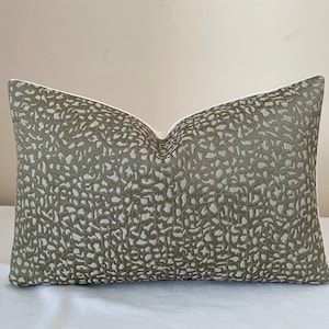May include: A rectangular decorative pillow with a white interior and a patterned exterior. The exterior features a repeating pattern of olive green and off-white shapes. The pillow is approximately 20 inches long and 12 inches wide.