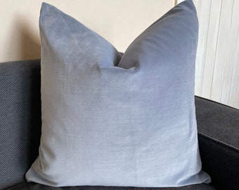 Peut inclure: Un coussin carré en velours bleu clair repose sur un canapé gris foncé. Le coussin a un aspect doux et texturé et est rempli pour créer une forme rebondie et accueillante. Le coussin est de couleur unie et ajoute une touche d'élégance.