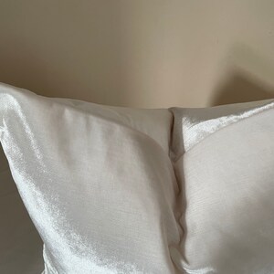 May include: Close-up of a white satin pillow. The pillow has a soft, lustrous sheen and a smooth texture. The pillow is a light cream color and appears to be new.