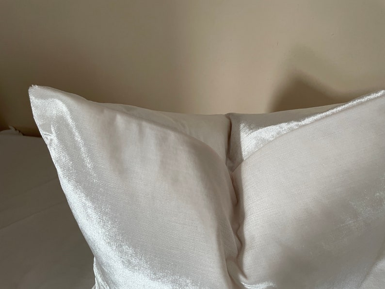 May include: Close-up of a white satin pillow. The pillow has a soft, lustrous sheen and a smooth texture. The pillow is a light cream color and appears to be new.