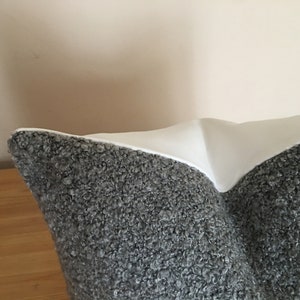 May include: A decorative pillow with a textured gray fabric on the bottom half and a smooth white fabric on the top half. The pillow is resting on a wooden surface.