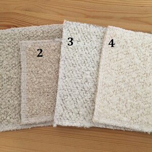 May include: Four rectangular, textured cloths in varying shades of off-white and beige are arranged on a wooden surface. The cloths have a looped, plush texture and are numbered 1 through 4.
