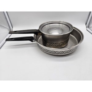 May include: Two stainless steel pots with black handles. The smaller pot has a lid and both pots have a decorative black and gold swirl design around the rim.