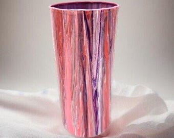 May include: A tall, cylindrical vase with a pink, purple, and white marbled design. The vase is made of glass or ceramic and has a smooth, glossy finish.