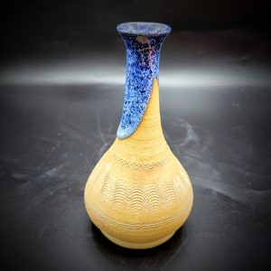 May include: A small, ceramic vase with a blue and yellow glaze. The vase has a narrow neck and a rounded body with a wavy pattern.