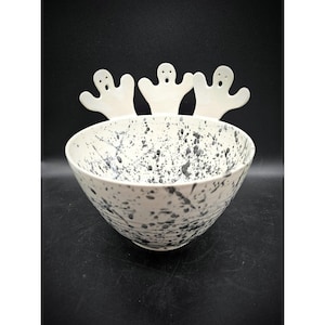 Op de afbeelding: Witte keramische kom met een zwart splatter-ontwerp. Drie witte keramische spookfiguren zitten op de rand van de kom.
