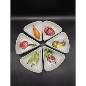 May include: Set of six white ceramic serving dishes shaped like pie slices. Each dish features a different hand-painted vegetable design, including carrots, tomatoes, radishes, peas, and mushrooms.