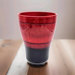 May include: A glossy, two-toned ceramic vase. The upper portion is a vibrant red, transitioning to a deep navy blue at the base. The vase has a cylindrical shape with a slightly flared top, and is approximately 8 inches tall.