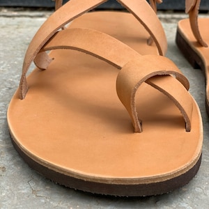 Pu&ograve; includere: Sandali in pelle color cuoio con pi&ugrave; cinturini che si incrociano sul piede. I sandali hanno una suola in pelle marrone.