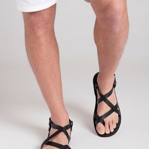 Pu&ograve; includere: Sandali in pelle nera con pi&ugrave; cinturini che si incrociano sul piede. I sandali hanno un passante per le dita e un cinturino alla caviglia.