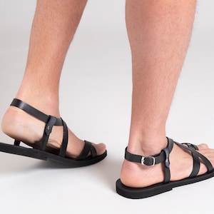 Pu&ograve; includere: Un paio di sandali in pelle nera con chiusura a fibbia. I sandali hanno un design semplice con cinturini incrociati.