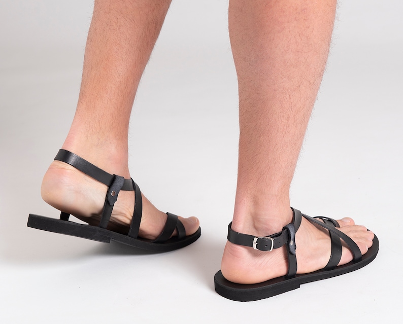 Pu&ograve; includere: Un paio di sandali in pelle nera con chiusura a fibbia. I sandali hanno un design semplice con cinturini incrociati.