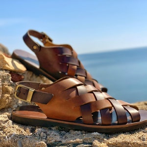 Puede incluir: Un par de sandalias de cuero marr&oacute;n con un dise&ntilde;o tejido. Las sandalias tienen un cierre de hebilla y una suela gruesa.